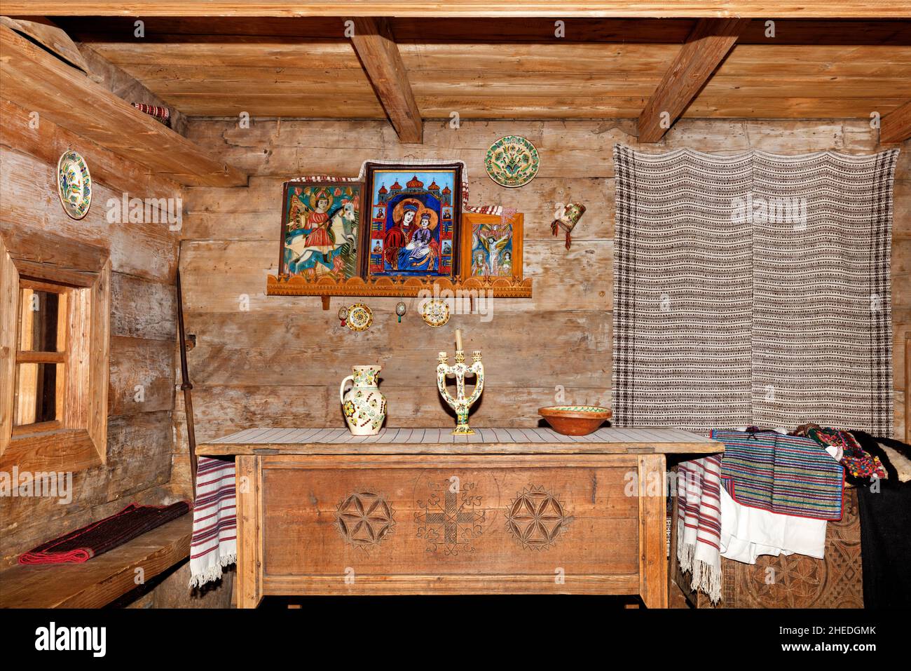 Das Innere des Wohnzimmers einer alten ukrainischen ländlichen Hütte mit heiligen Bildern über einem geschnitzten Esstisch und bestickten Leinentüchern. Stockfoto