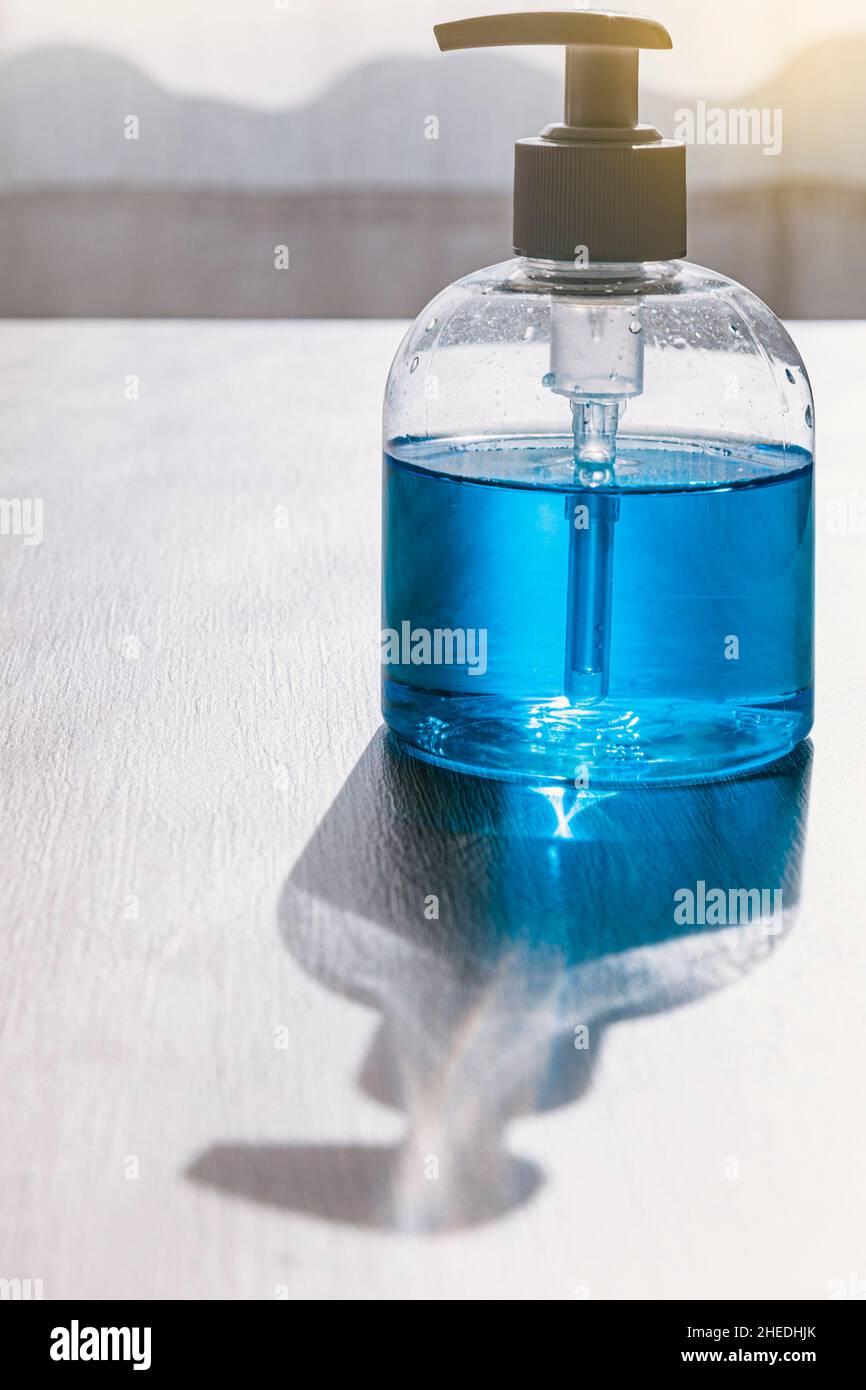 Auf einem Holztisch befindet sich eine Flasche mit einem Spender aus hydroalkoholischem Gel oder blauer Seife. Das Licht kommt von vorne intensiv und wirft den Schatten o Stockfoto