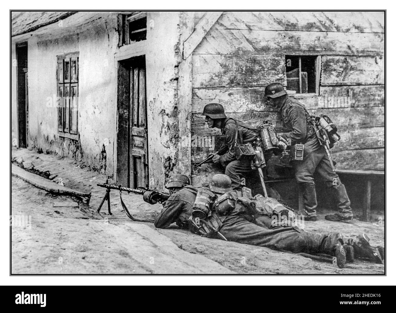 Operation Barbarossa WW2 Straßenkämpfe in einem Dorf an der Ostfront. Vier Nazi-deutsche Soldaten verstecken sich hinter der Ecke des Hauses. Nazi-deutscher Soldat mit MG-34-Maschinengewehr im Vordergrund. Stockfoto