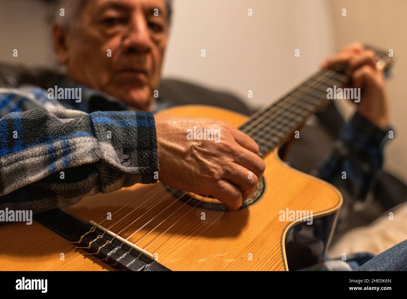 Alter Mann spielt akustische Gitarre und sitzt auf dem Sofa Stockfoto
