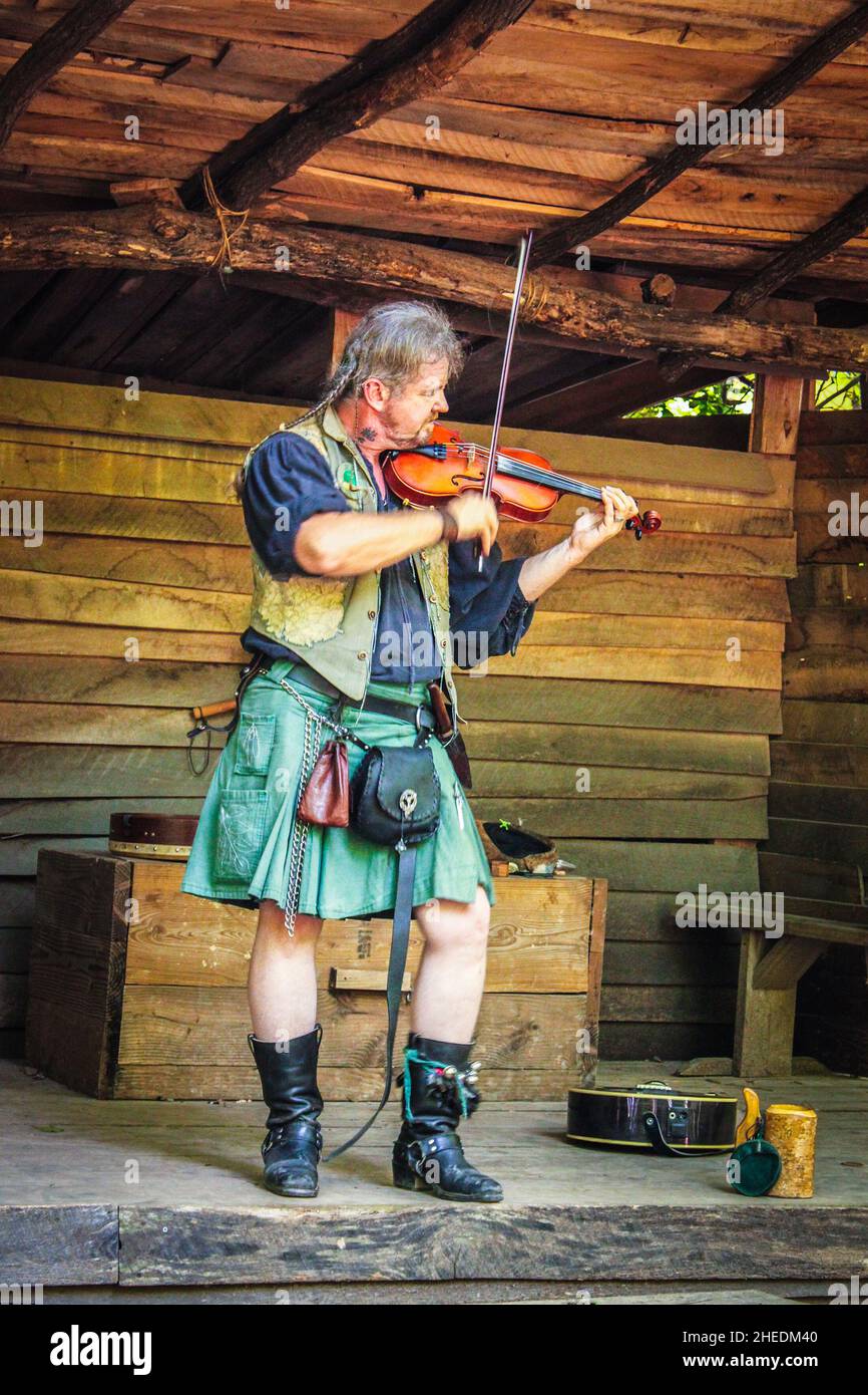 05-2016 Muskogee USA Mann im grünen Kilt mit Zöpfen und Taschen spielt Geige auf rustikaler Holzbühne - Motion Blur Stockfoto