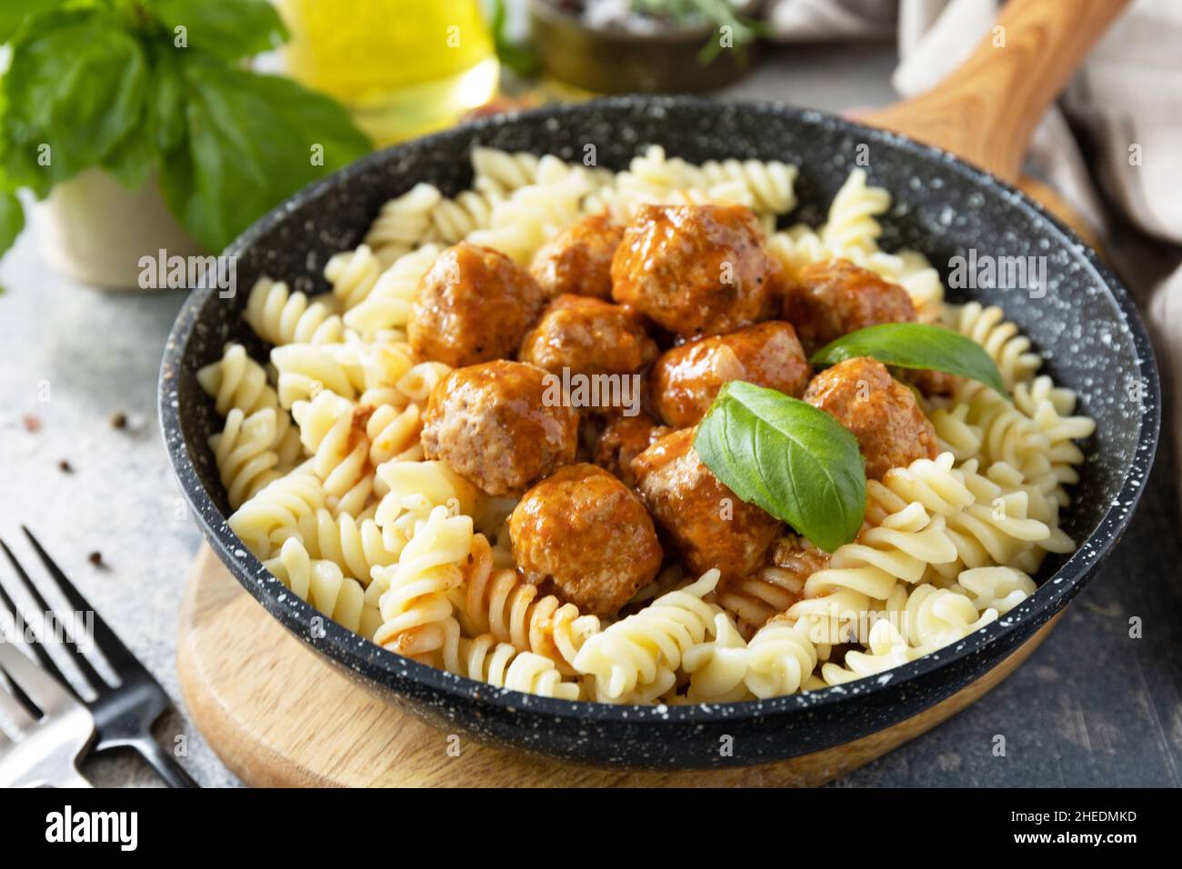 Italienische Küche. Italienische Fusilli-Pasta mit Fleischbällchen in Tomatensauce und Basilikum auf grauem Steingrund. Stockfoto