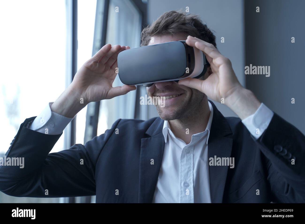 Aufgeregter Geschäftsmensch in Anzug, der ein VR-Headset am Kopf trägt und an Meetings in der virtuellen Realität teilnimmt Stockfoto