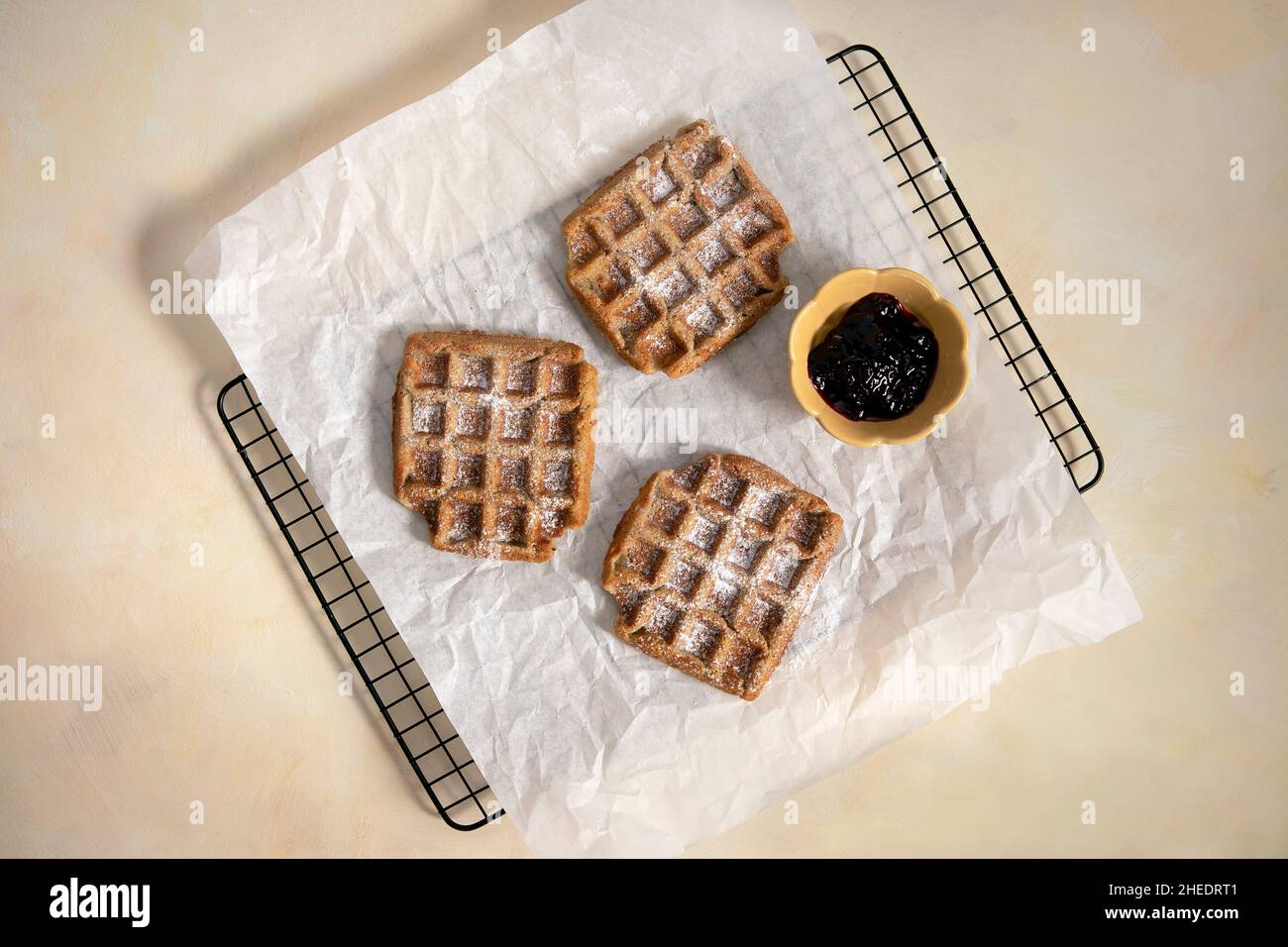 Frisch gebackene Waffeln von oben. Draufsicht auf vegane, glutenfreie Waffeln mit Marmelade und Puderzucker auf gelbem Hintergrund. Leckeres hausgemachtes Dessert. Stockfoto