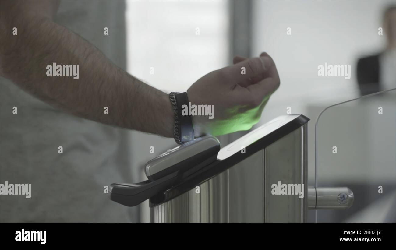 Mann, der ein RFID-Armband an der elektronischen Zugangsausrüstung am Eingangstor zur U-Bahn, U-Bahn oder Fitnessstudio angebracht hat. Rahmen. Schwarzes elektronisches Armband für Stockfoto