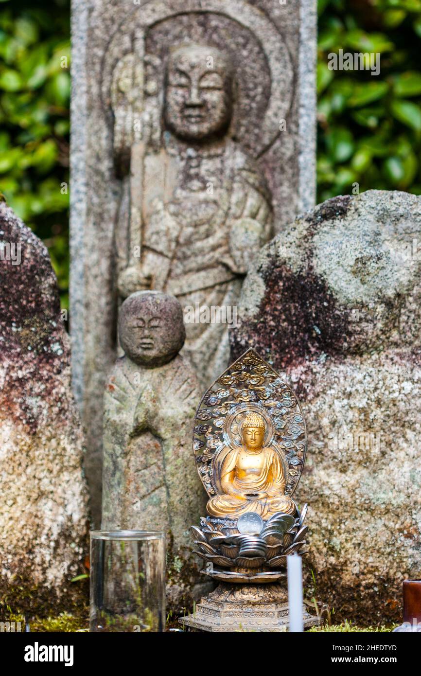 Kleine buddha-Statue mit Münzopfern zu Füßen, dahinter zwei größere Jizo-Statuen, beide außer Fokus, im Saisho-in Garden, Nanzen Tempel. Kyoto Stockfoto