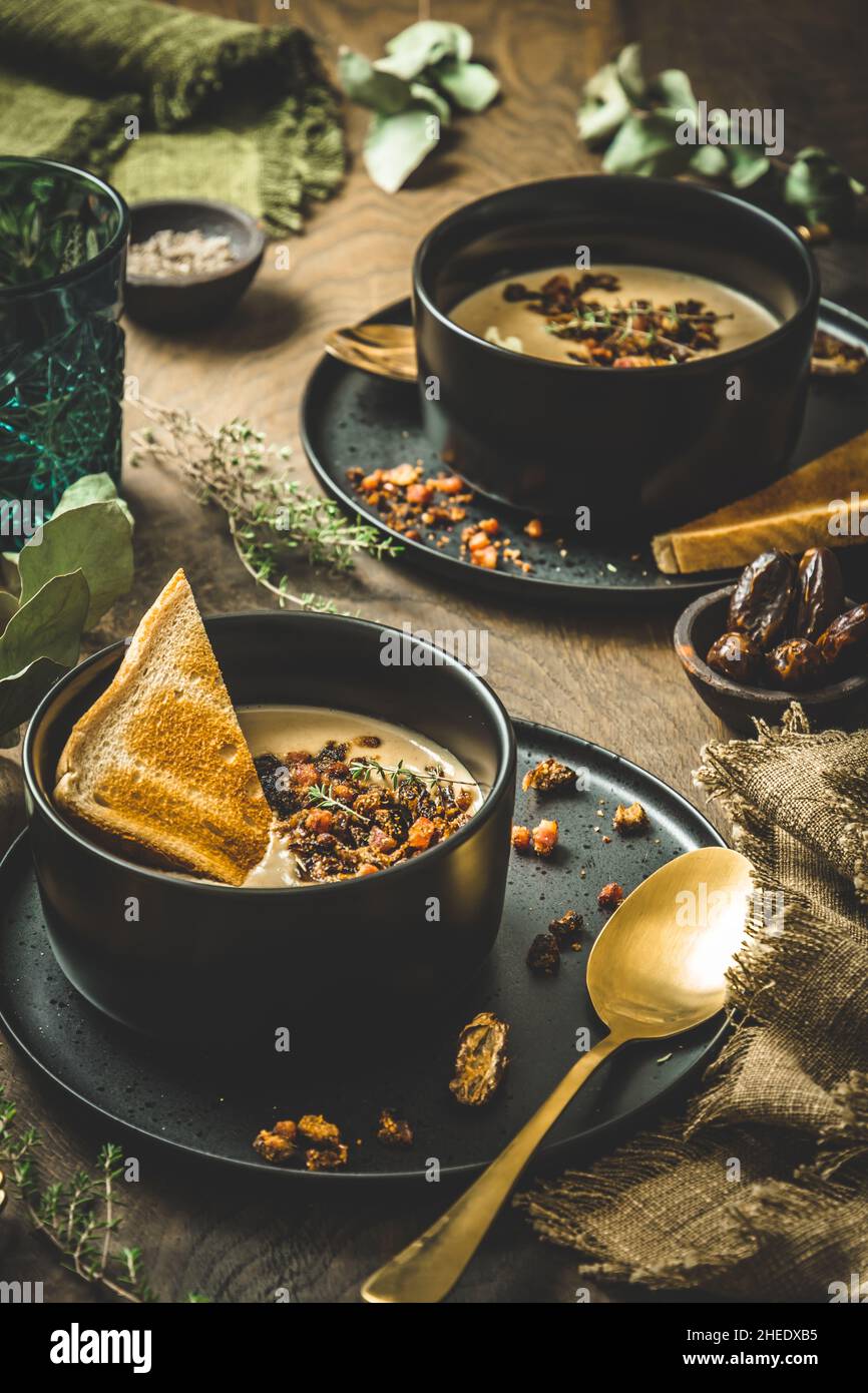 Kastaniensuppe mit rotiertem Belag, Creme und Brot in einer schwarzen Schüssel auf rustikalem Holzhintergrund, vertikal Stockfoto