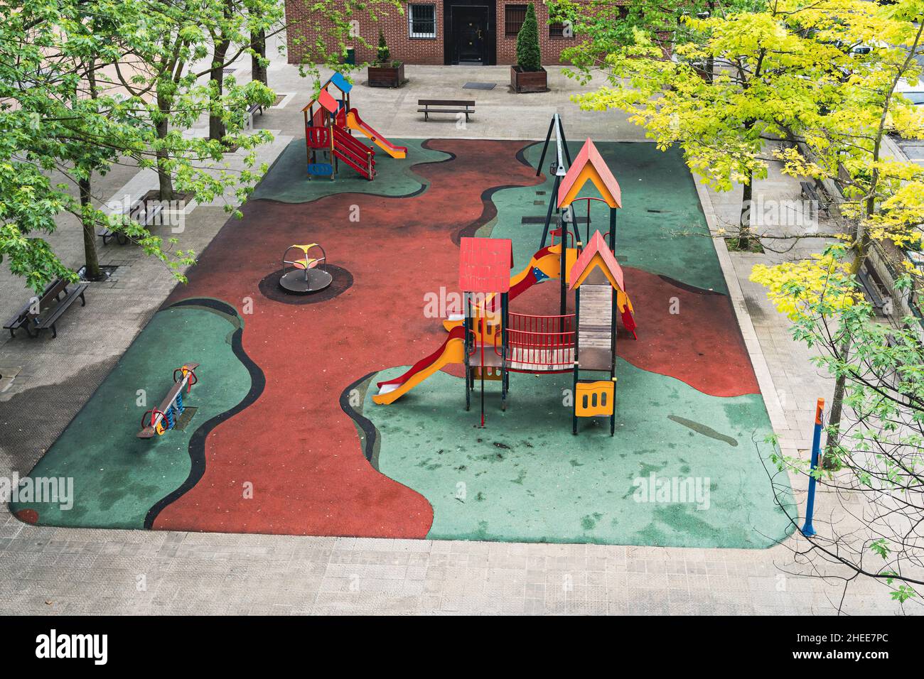 Leerer Spielplatz für Kinder mit Schaukeln und Rutschen auf einem gepolsterten, von Bäumen gesäumten Boden. Pandemische Quarantäne, niemand im Freien Konzepte Stockfoto