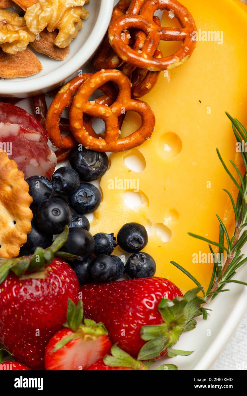 Blick von oben auf den leckeren Aufschnitt mit verschiedenen Käsesorten und Nüssen, serviert mit reifen Erdbeeren auf dem Tisch in der hellen Küche Stockfoto