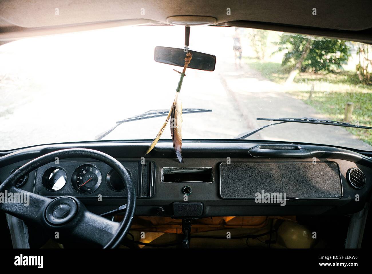 Schwarzes Lenkrad mit Armaturenbrett und dekorativen Federn auf Spiegel in alten Timer-Automobil mit klarer Windschutzscheibe auf Asphalt geparkt Straße Stockfoto