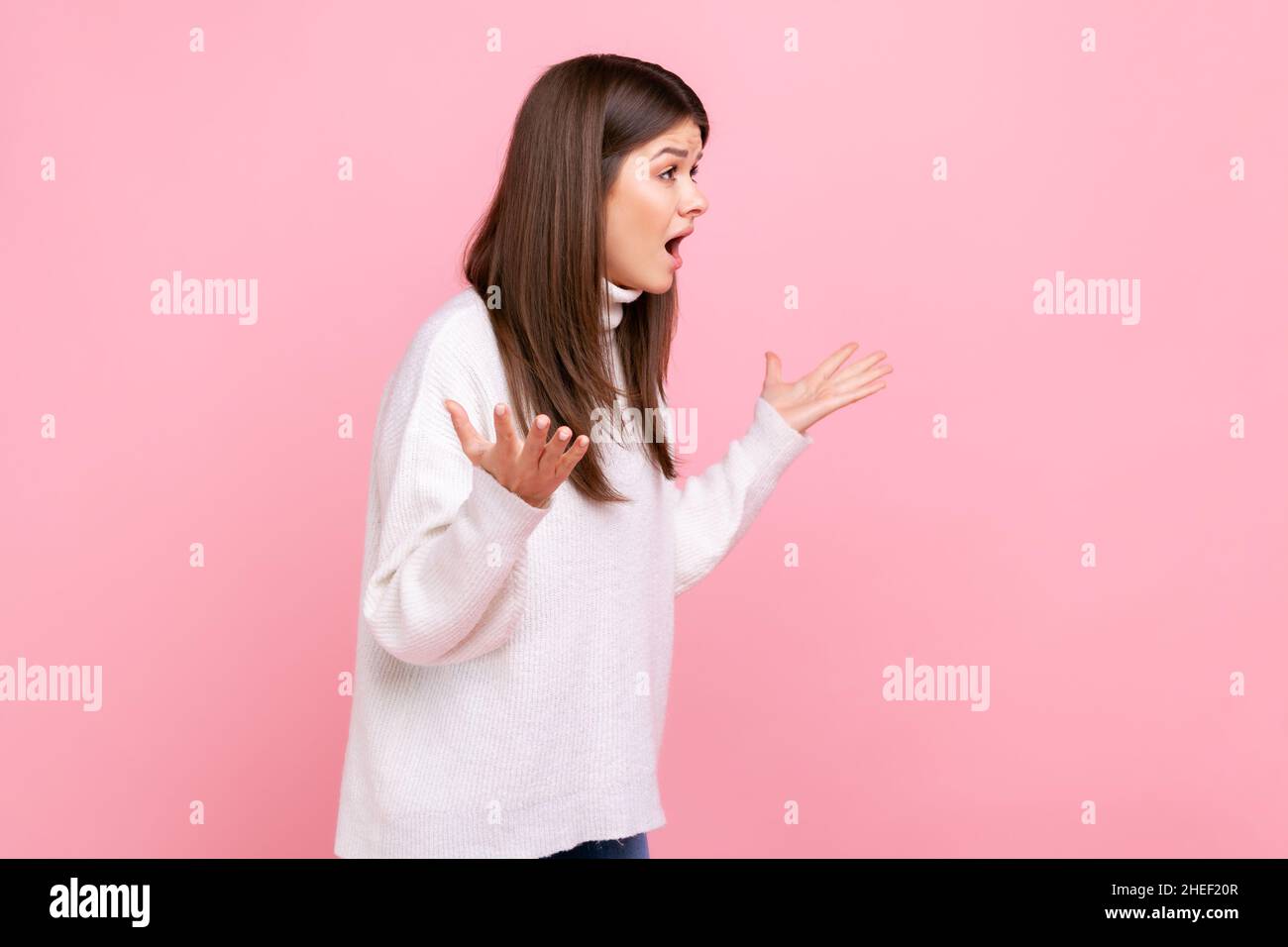 Seitenansicht Porträt eines jungen Mädchens, das in wütender Geste die Hände hält, vor Wut und Wut schreit und einen weißen Pullover im lässigen Stil trägt. Innenaufnahme des Studios isoliert auf rosa Hintergrund. Stockfoto