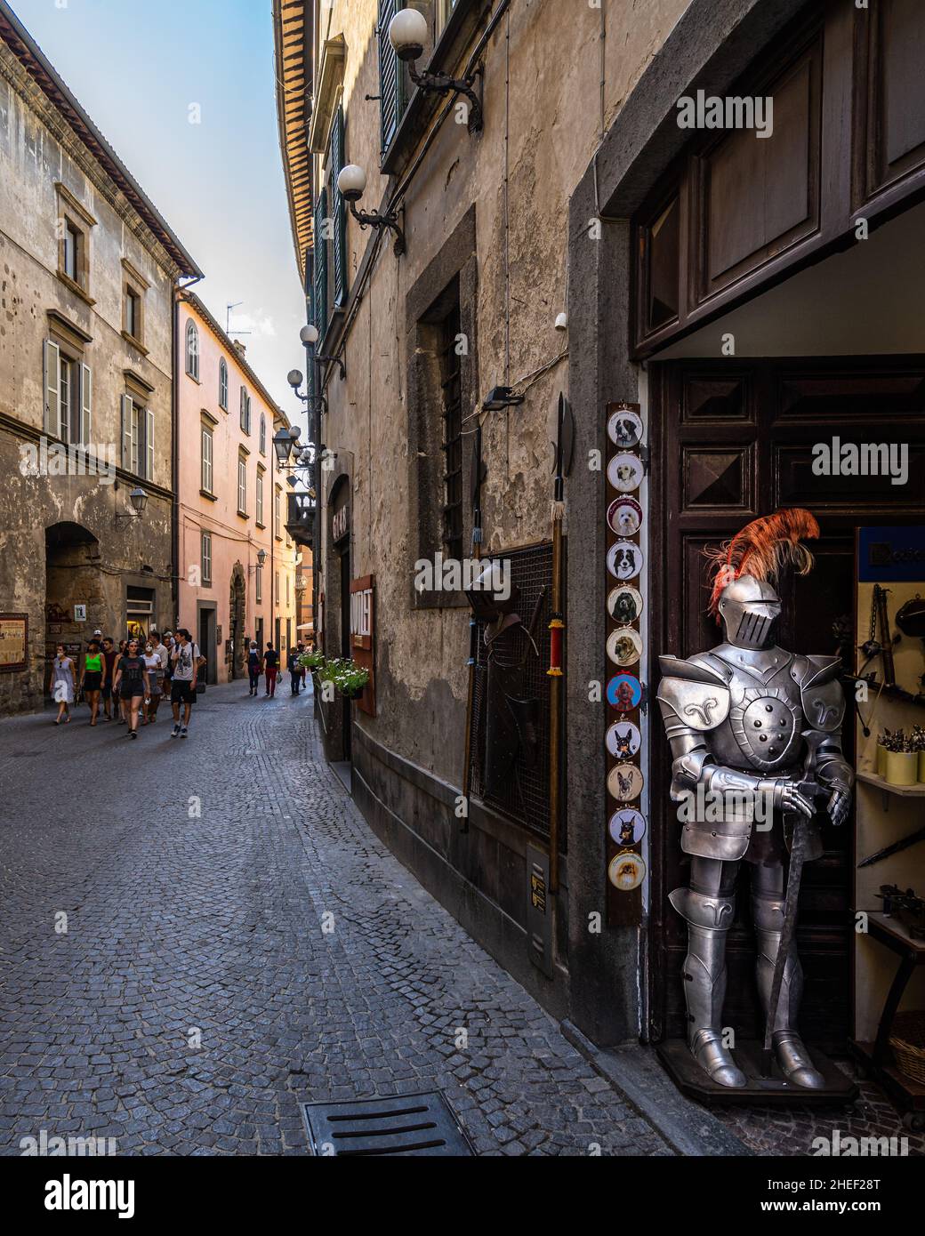 Orvieto, Umbrien, 2021. August – Fußgängerzone im historischen Zentrum von Orvieto mit einer mittelalterlichen Rüstung, die in einem Souvenirladen ausgestellt ist. Stockfoto