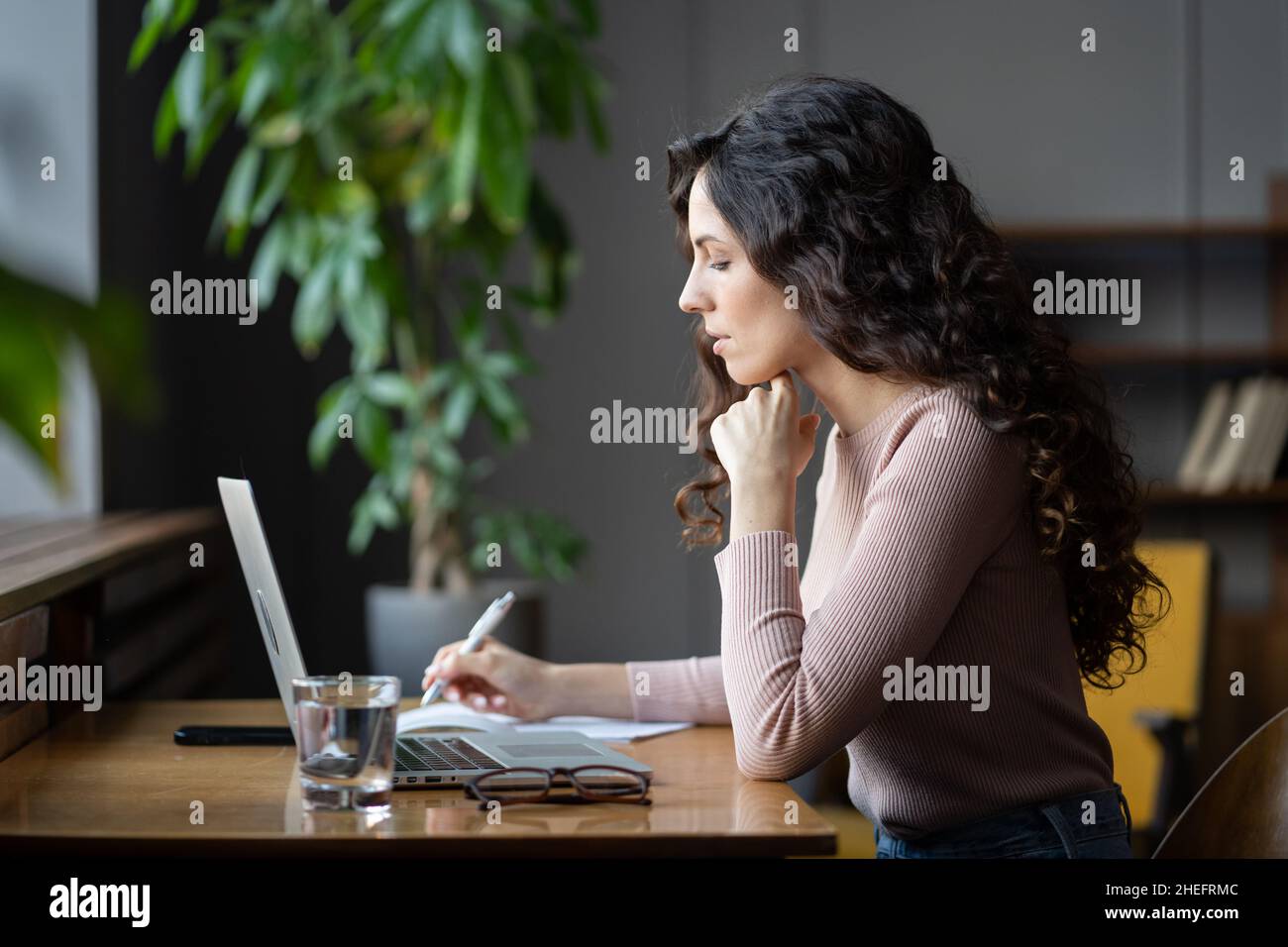 Junge Akademikerin, die sich den Laptop-Bildschirm ansieht, recherchiert online, während sie in der Bibliothek arbeitet Stockfoto