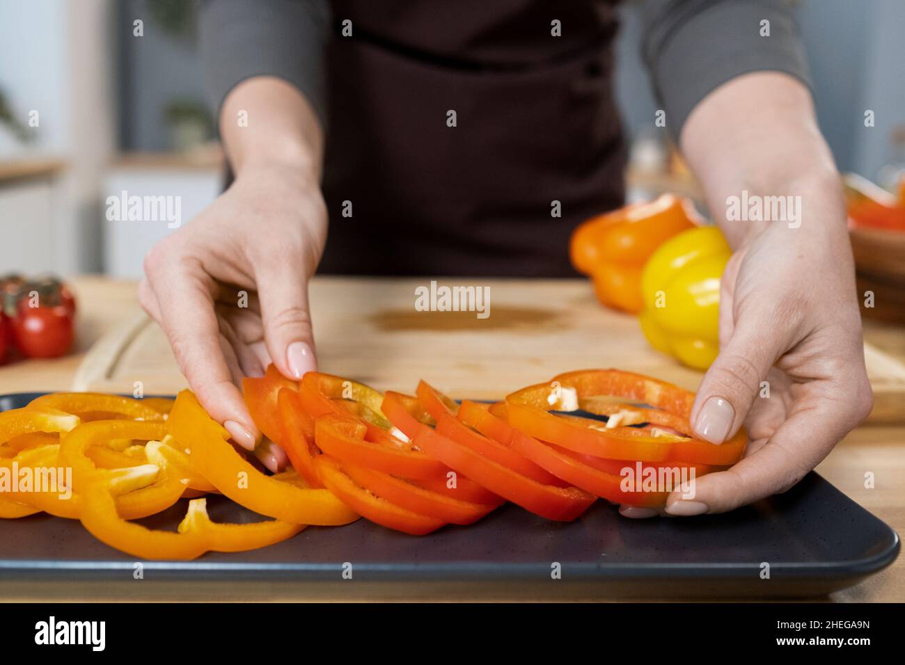 Hände junger Frauen, die frischen, gehackten Pfeffer auf das Tablett legen, während sie am Küchentisch stehen und vegetarisches Essen kochen Stockfoto
