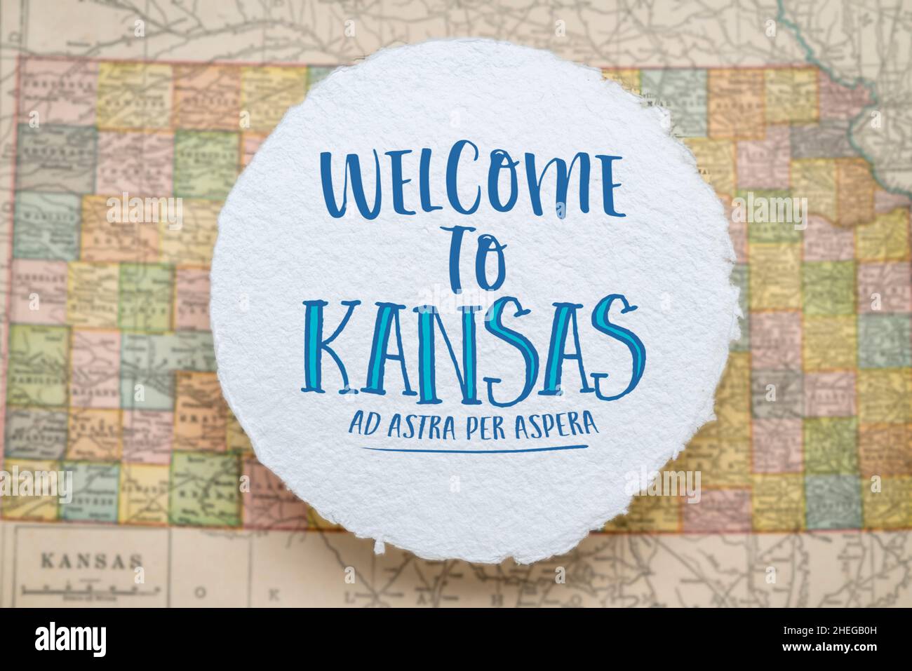 Willkommen in Kansas, ad astra per aspera - Handschrift auf einem kreisförmigen Blatt aus rohem, handgefertigtem Papier, das über einer Vintage-Unschärfe-Karte von Kansas, hospit, schwebt Stockfoto