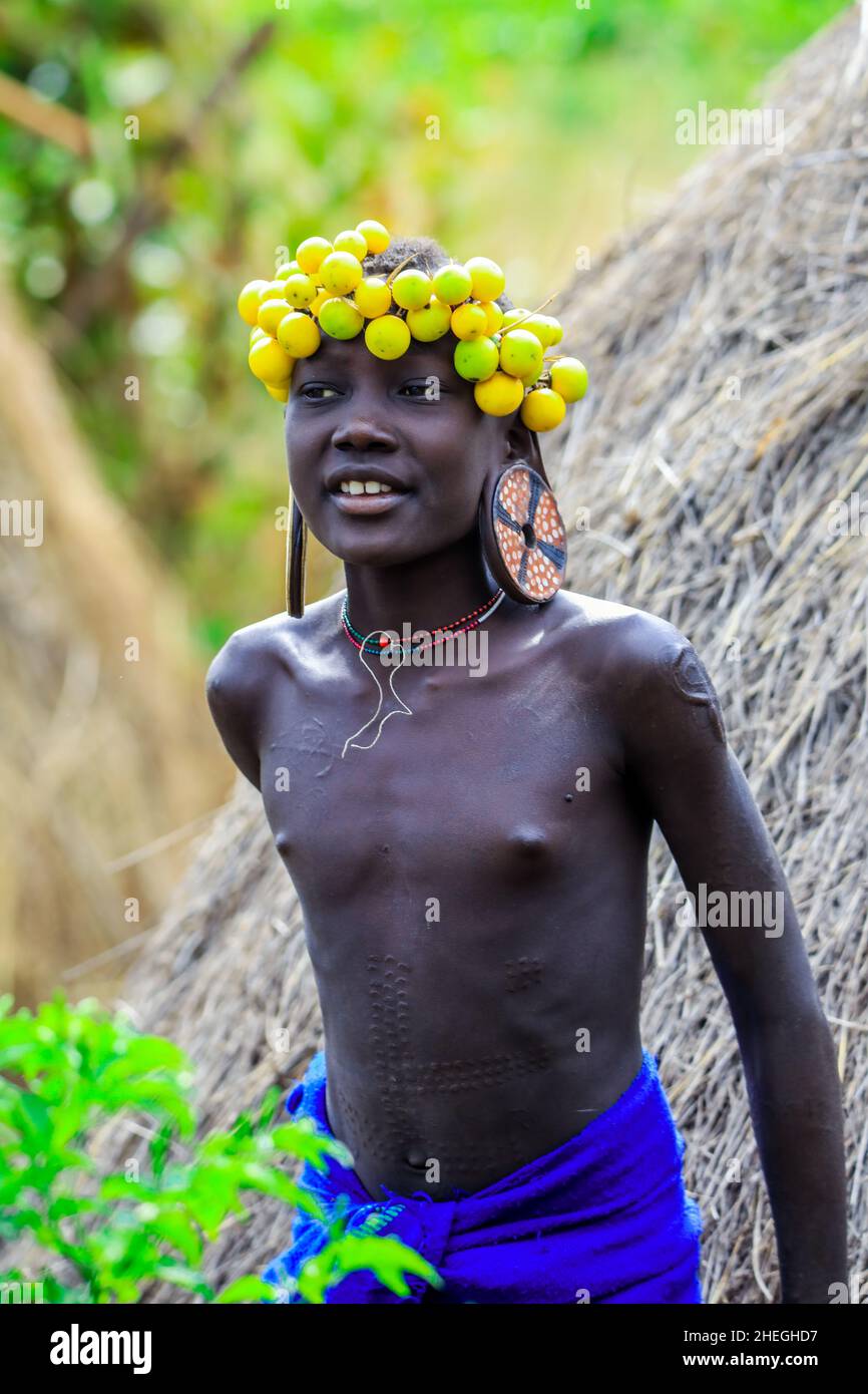 Omo River Valley, Äthiopien - 29. November 2020: Porträt eines afrikanischen Teenagers mit großen traditionellen hölzernen Ohrringen und einem Kranz aus trockenen gelben Blumen Stockfoto