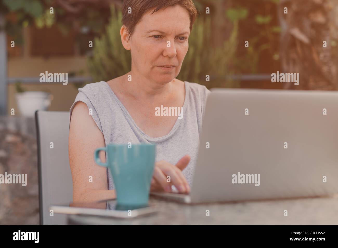 Seriöse freiberufliche Frau und digitale Nomade arbeiten auf Laptop-Computer während der Sommerferien Urlaub auf der Terrasse der Wohnung am Morgen Stockfoto