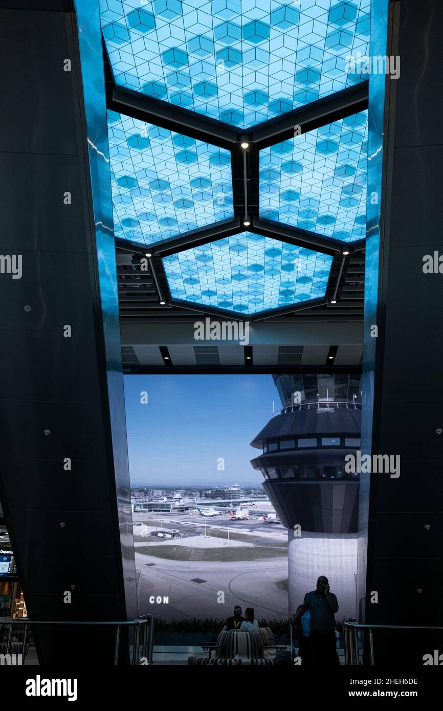 Passagiere, die vor einem großen digitalen Werbebildschirm in der Abflughalle am Flughafen Manchester, England, vorbeikommen Stockfoto
