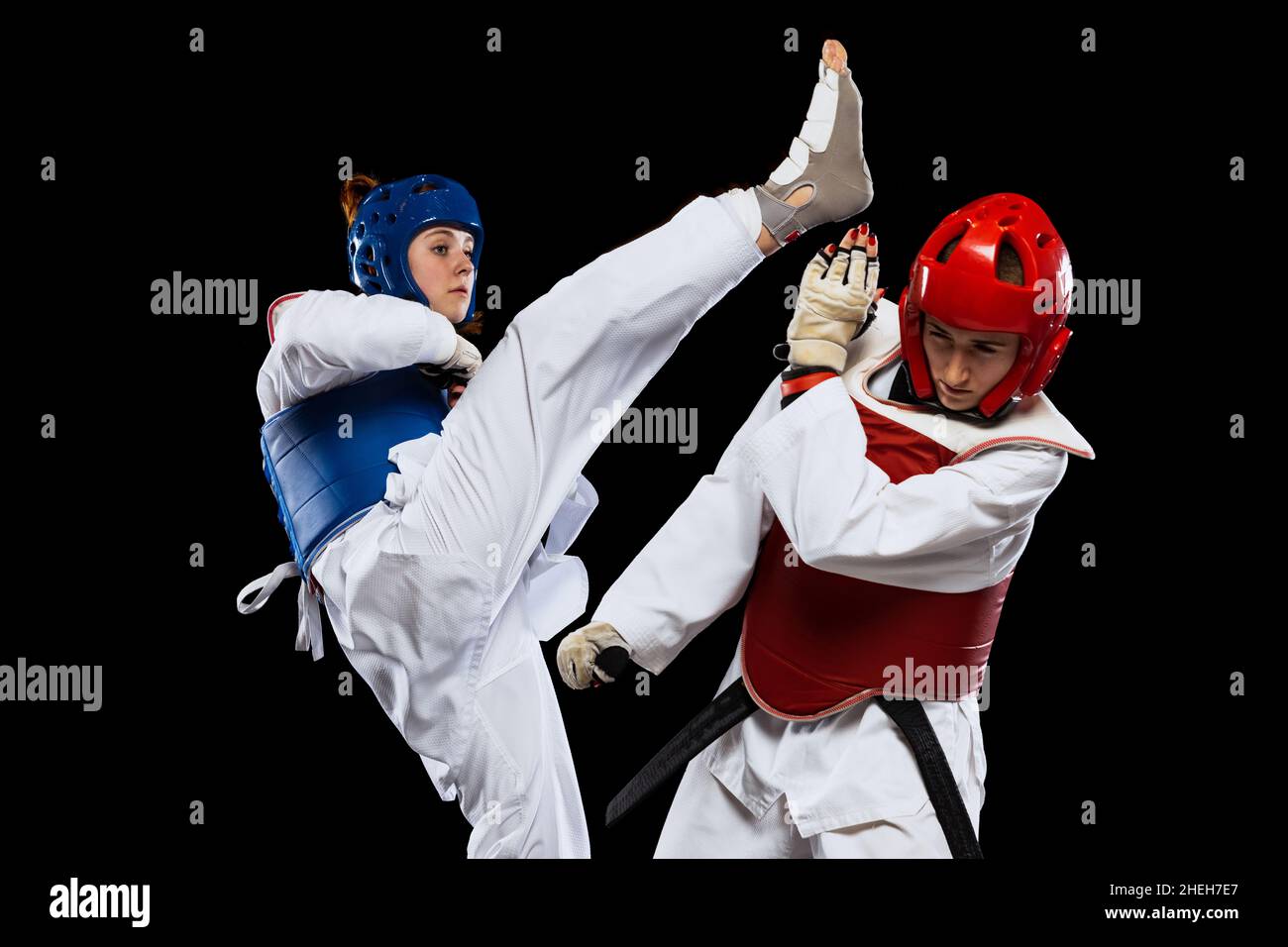 Dynamisches Porträt von zwei weiblichen Taekwondo-Praktizierenden, die isoliert vor dunklem Hintergrund zusammen trainieren. Konzept des Sports, Fähigkeiten Stockfoto