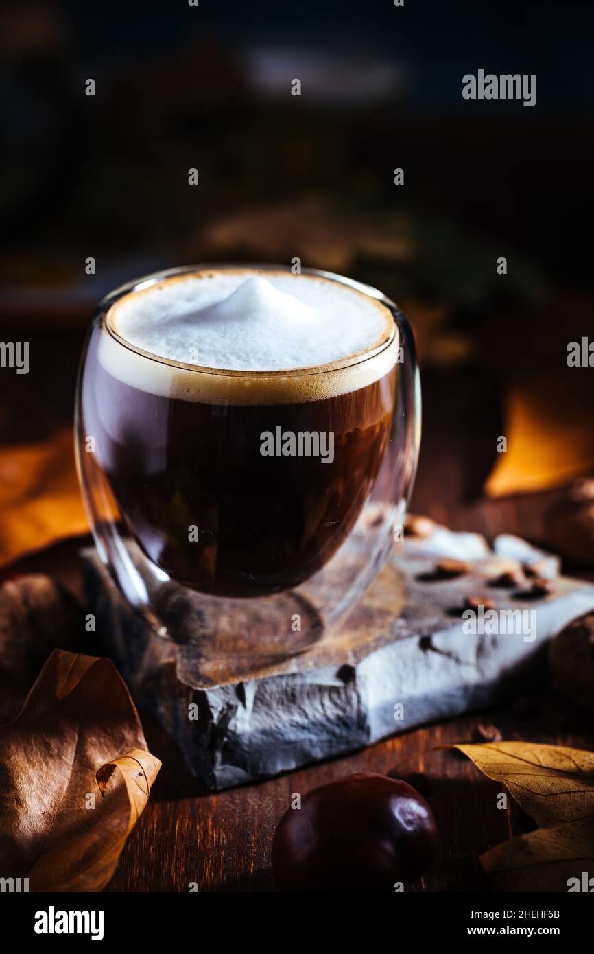 Tasse Kaffee in doppelter Glastasse in herbstlicher Stimmung mit Blättern und Kaffeebohnen Details in Einstellung und Hintergrund Stockfoto