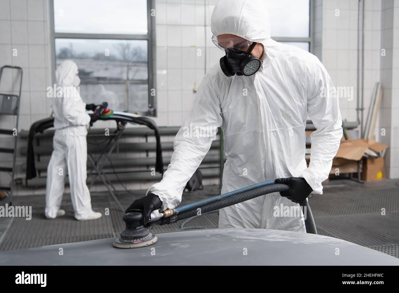 Arbeiter in Hazmat Anzug arbeiten mit Auto Polierer in der Garage Stockfoto
