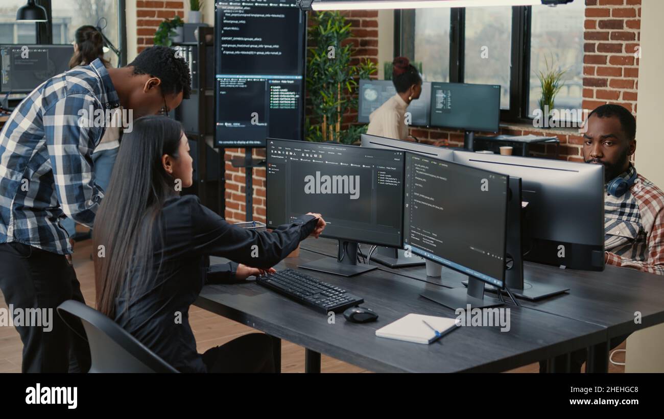 Gemischtes Team von Programmierern, die den Quellcode analysieren und auf Bildschirme zeigen, die den Algorithmus mit der Benutzeroberfläche auf einem digitalen Tablet vergleichen. Software-Entwickler arbeiten an Cyber-Security-Gruppe Projekt. Stockfoto