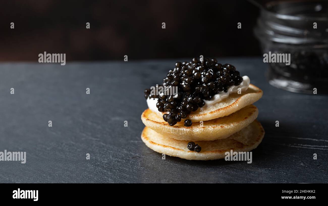 Schwarzer Kaviar auf einem Stapel Pfannkuchen auf dunkelgrauem Hintergrund mit Platz zum Kopieren Stockfoto