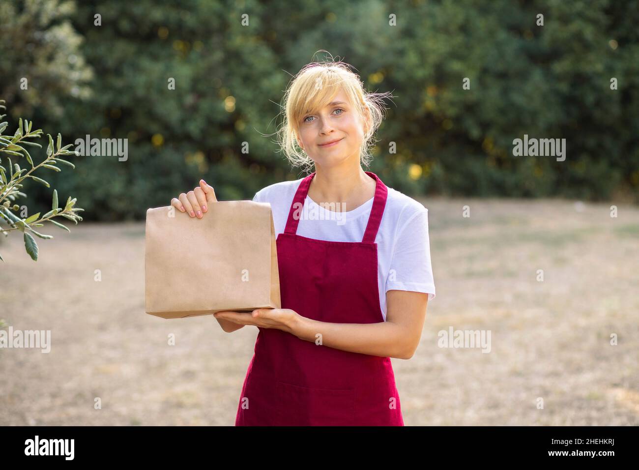 Frau in einer Schürze hält eine Papiertüte mit Öko-Produkten. Bio-Lebensmittel. Lieferung von Bio-Produkten vom Bauernhof. Stockfoto