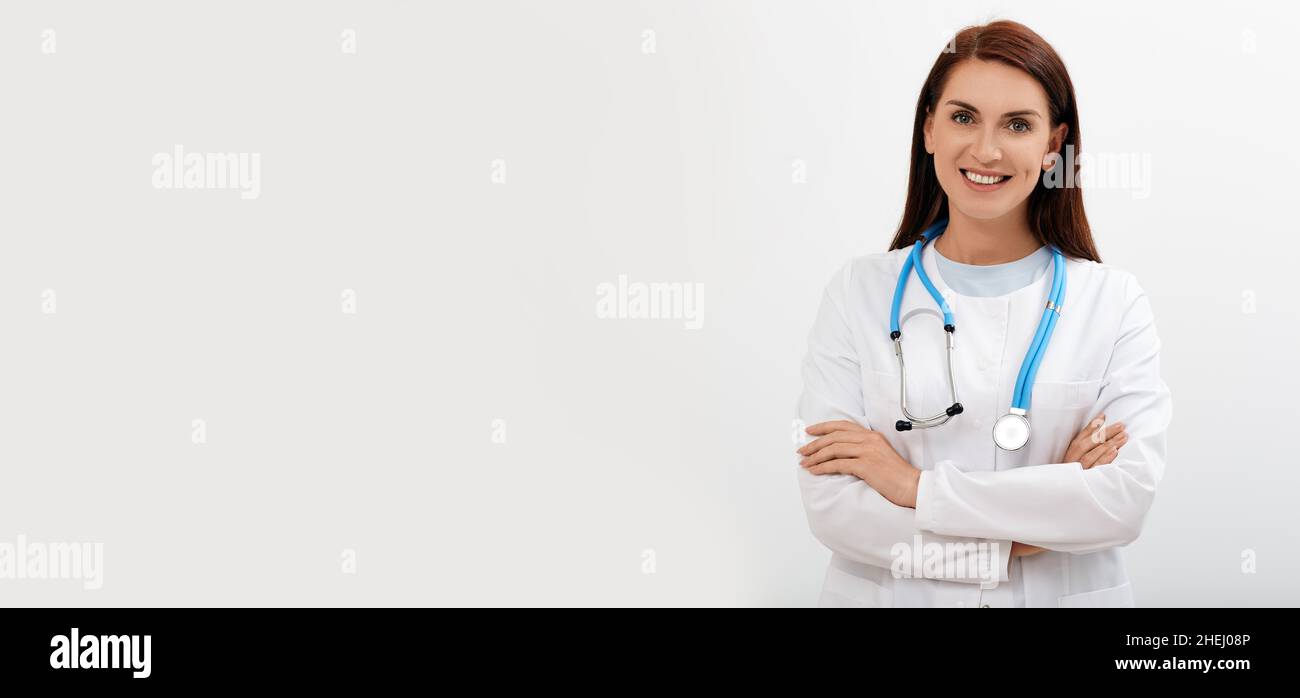Lächelnde Ärztin mit überkreuzten Armen stehend und in die Kamera schauend, isoliert auf weißem Hintergrund mit Platz für Text. Medizinisches Berufskonzept Stockfoto