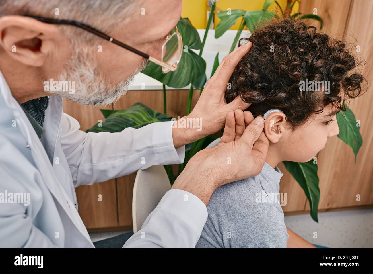 Gehörbehandlung, Hörlösungen für Kinder. Anbringen eines Hörgeräts am männlichen Kinderohr in der Hörklinik, Seitenansicht Stockfoto