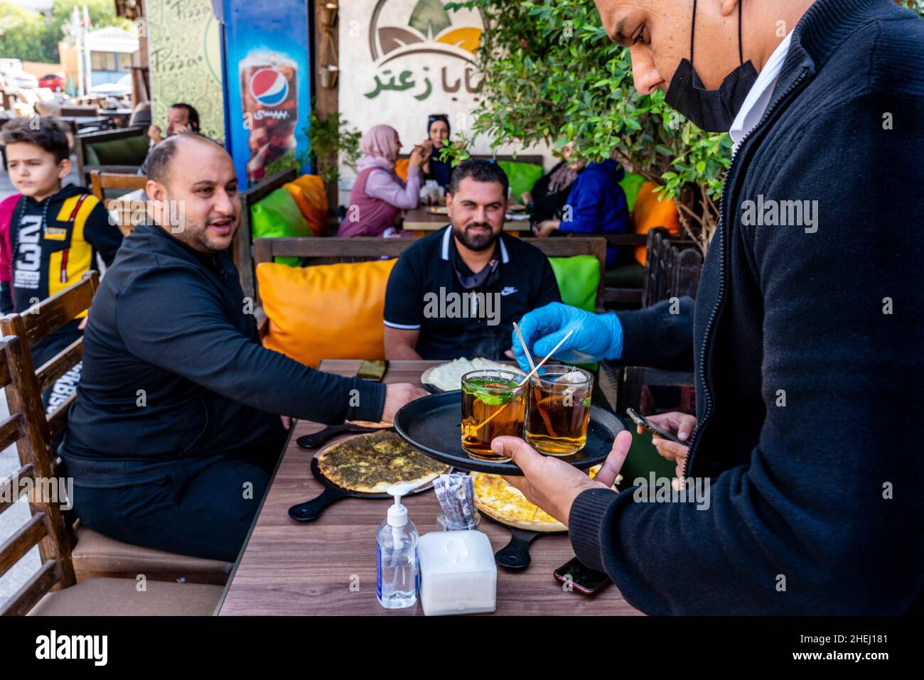Ein Kellner serviert Minztee für Eine Gruppe jordanischer Männer, die ein traditionelles Frühstück mit Fladenbrot essen, Aqaba, Aqaba Governorate, Jordanien. Stockfoto