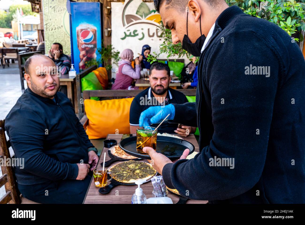 Ein Kellner serviert Minztee für Eine Gruppe jordanischer Männer, die ein traditionelles Frühstück mit Fladenbrot essen, Aqaba, Aqaba Governorate, Jordanien. Stockfoto