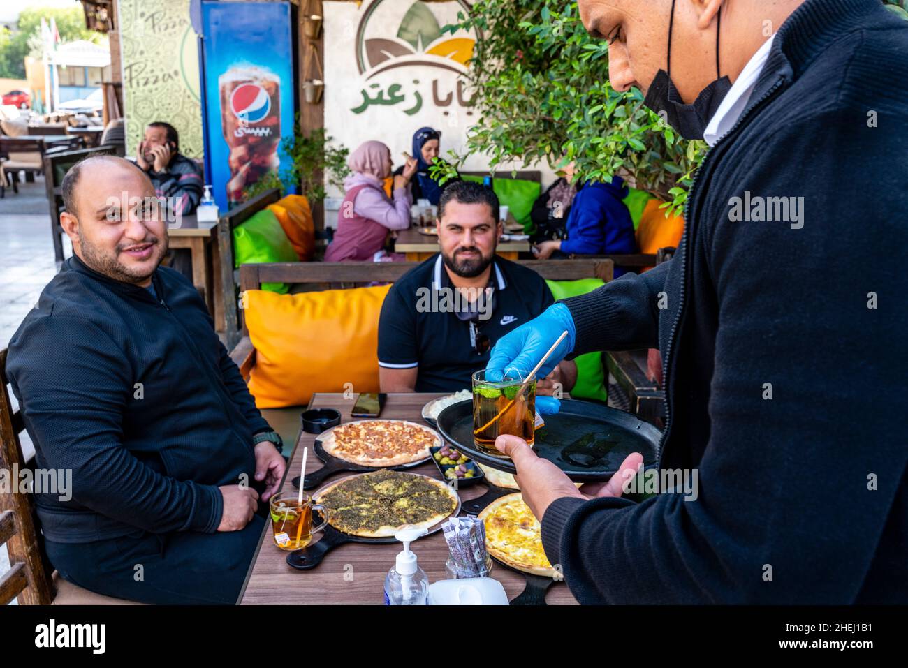 Ein Kellner serviert Minztee für Eine Gruppe jordanischer Männer, die ein traditionelles Frühstück mit Fladenbrot essen, Aqaba, Aqaba Governorate, Jordanien. Stockfoto