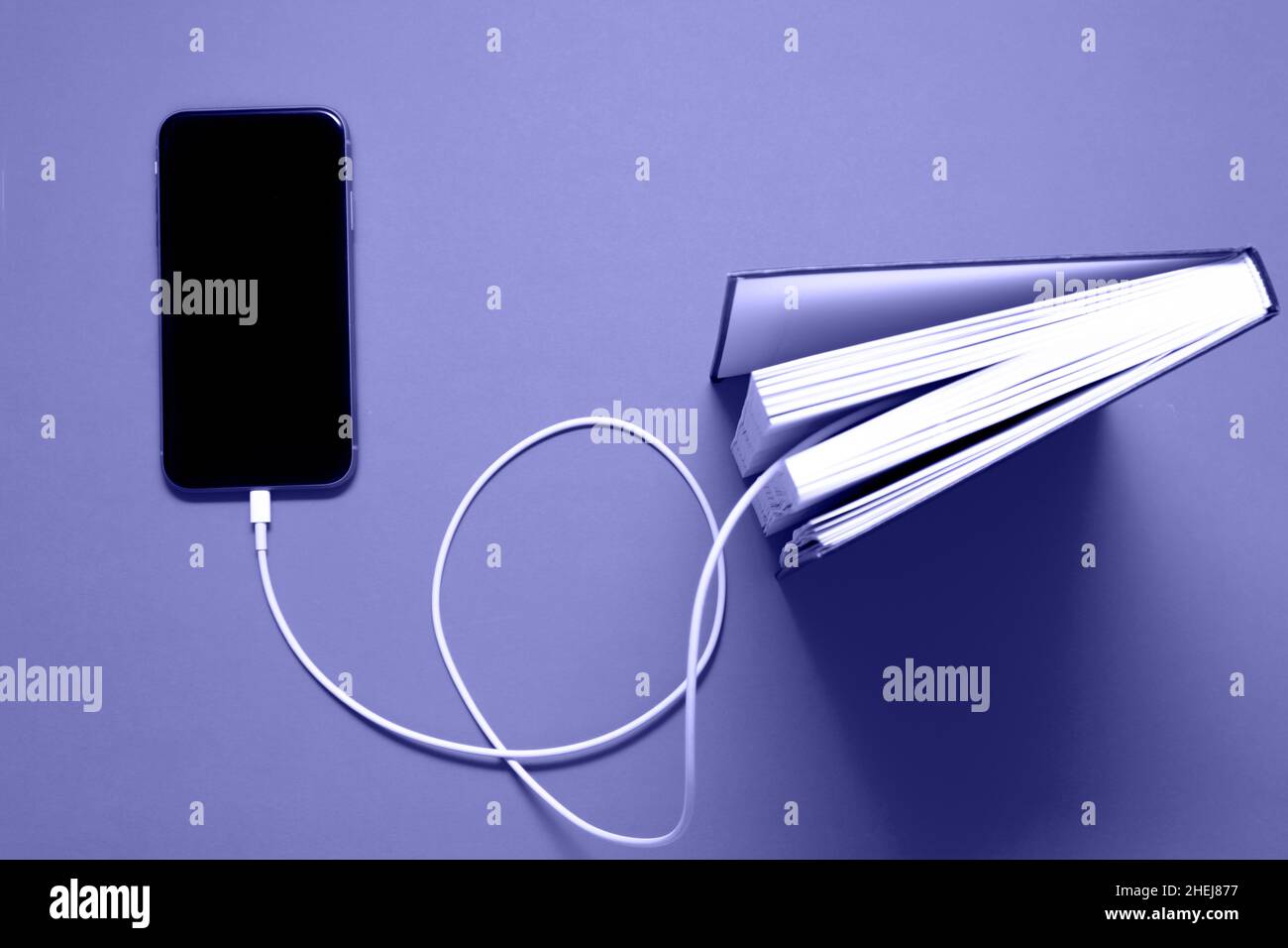 Das Smartphone verbindet sich mit einem Kabel mit dem alten Buch und lädt Informationen von dort herunter. Elektronische Informationen. Sehr reines Tonbild. Stockfoto