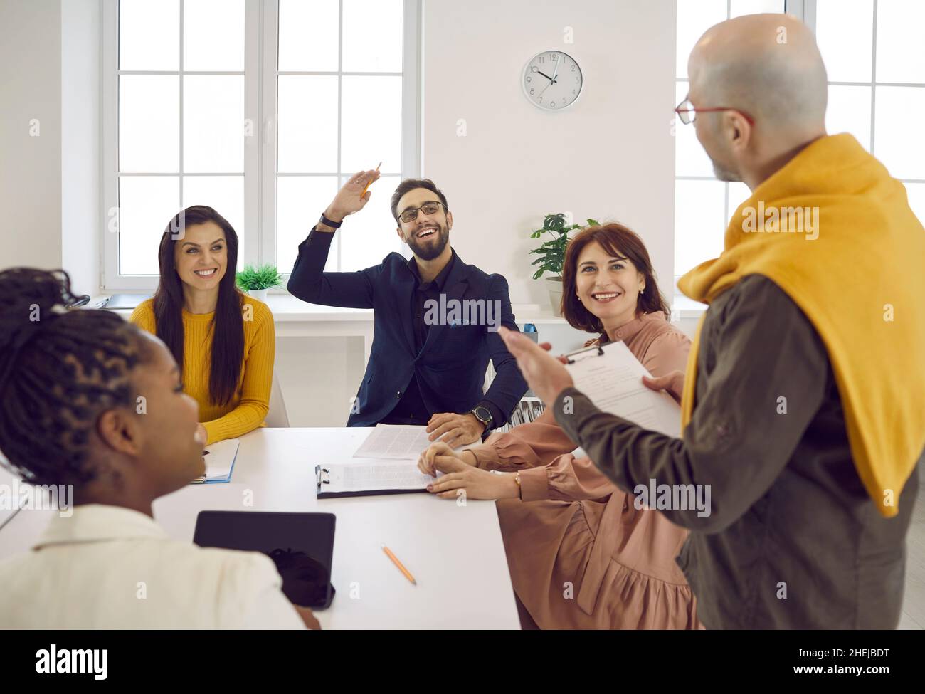 Glücklicher Mann hebt die Hand, um seinem Kollegen während eines Geschäftsmeeting eine Frage zu stellen Stockfoto
