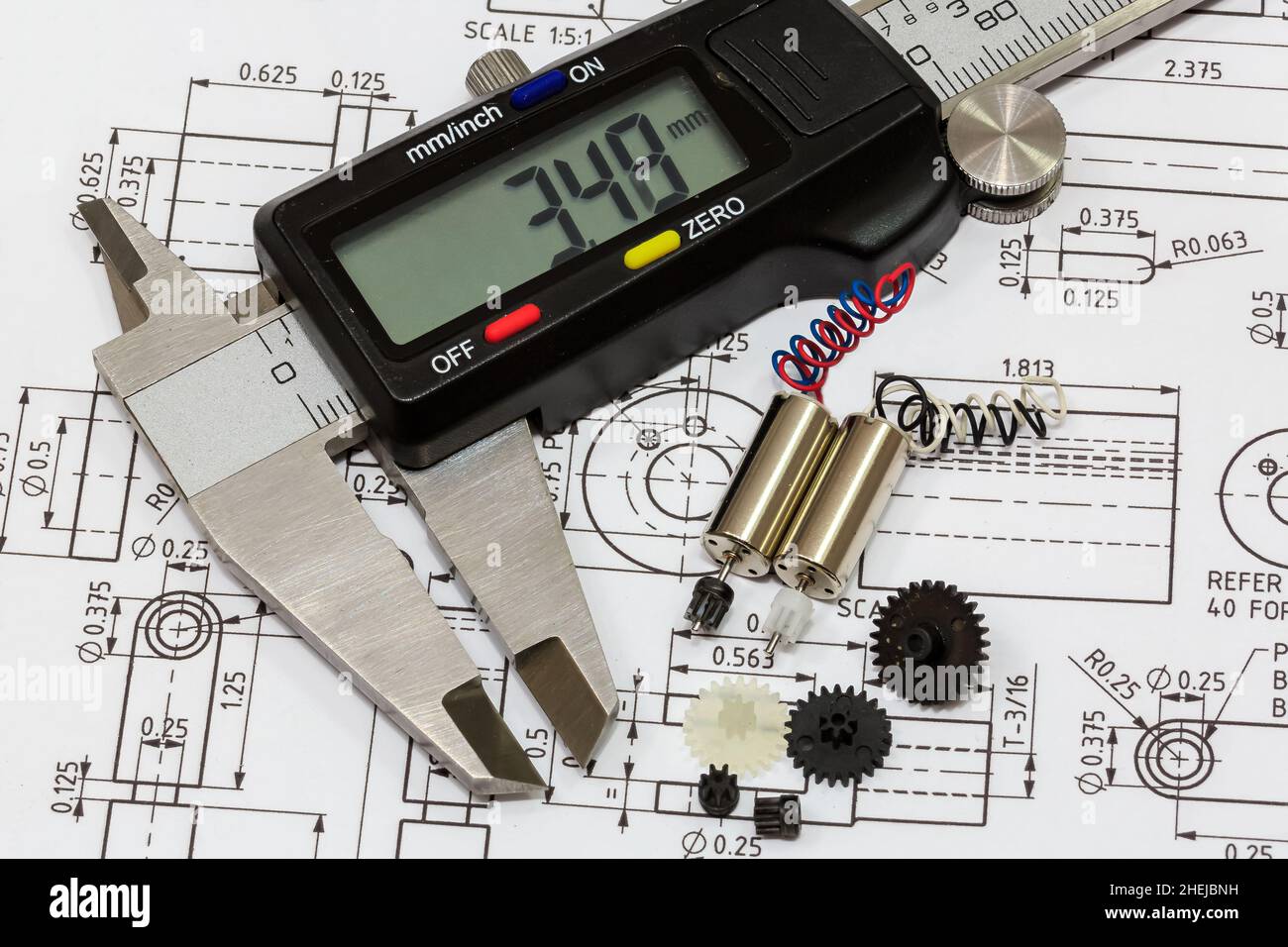 Nahaufnahme eines Miniatur-Elektromotors, Nylongetriebe und Messschieber auf einem Hintergrund mit technischen Zeichnungen Stockfoto