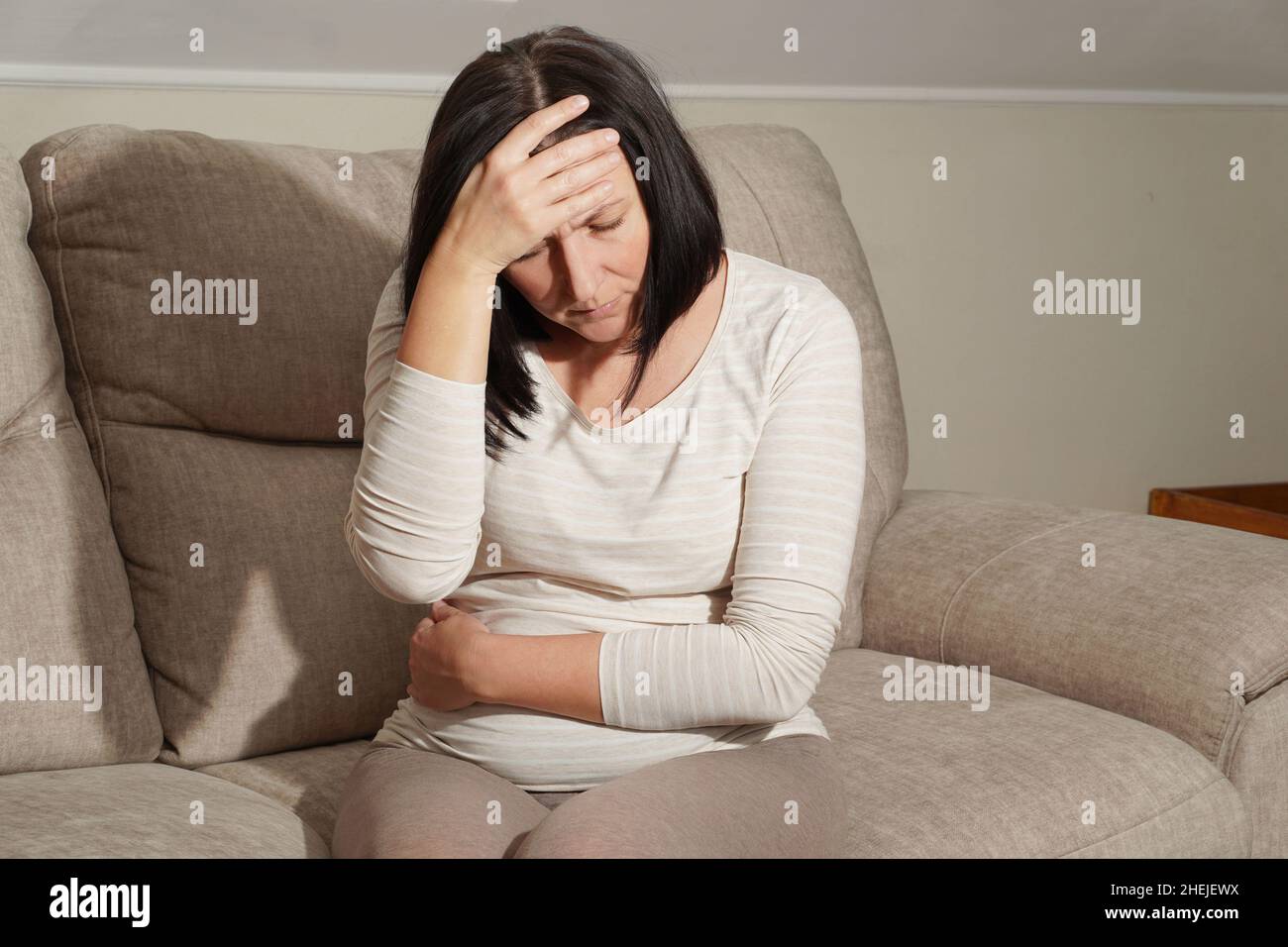 Reife Schwangere mittleren Alters, die an Kopfschmerzen und Magenschmerzen, Toxikose zu Hause leidet. Bauchschmerzen, Lebensmittelvergiftung, Durchfall, Magengeschwüre Stockfoto