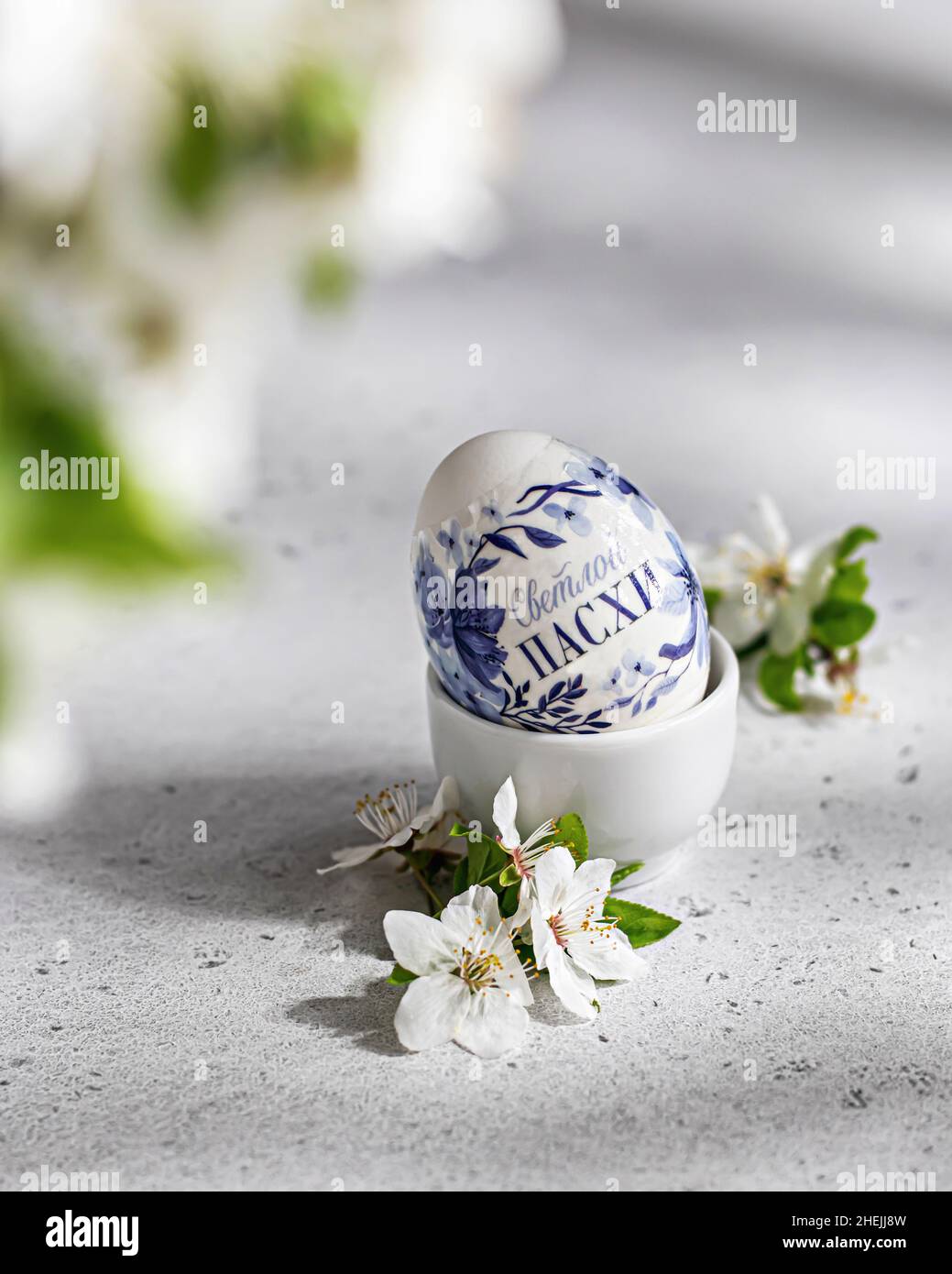 Osterkomposition mit farbigem Ei und blühenden Blumen auf weißem strukturiertem Hintergrund Stockfoto