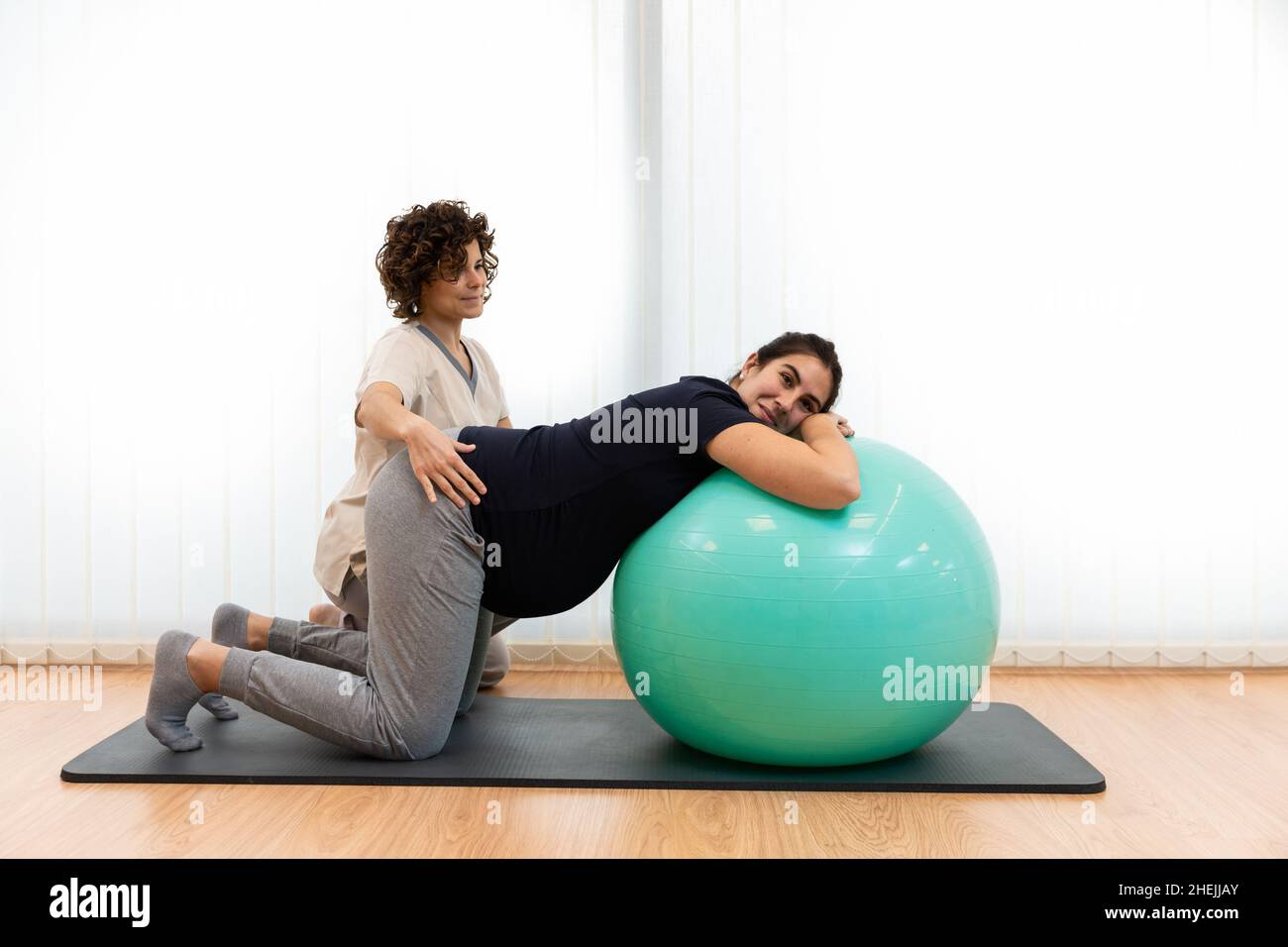 Eine Schwangerin macht Atemübungen und ruht sich mit Hilfe ihres Physiotherapeuten auf einem Fitnessball aus Stockfoto
