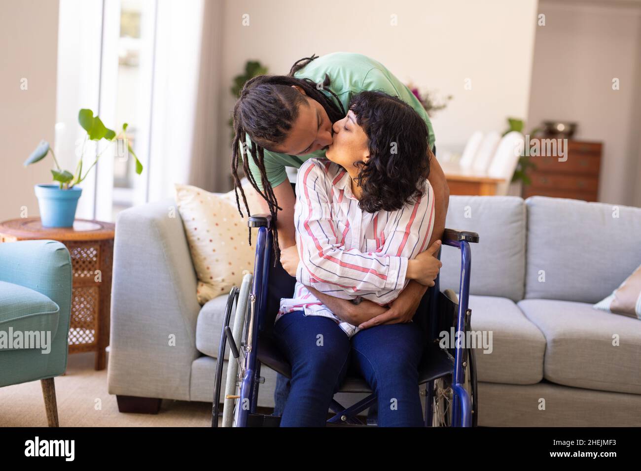 afroamerikanischer Mann umarmt und küsst seine behinderte Frau zu Hause im Rollstuhl Stockfoto