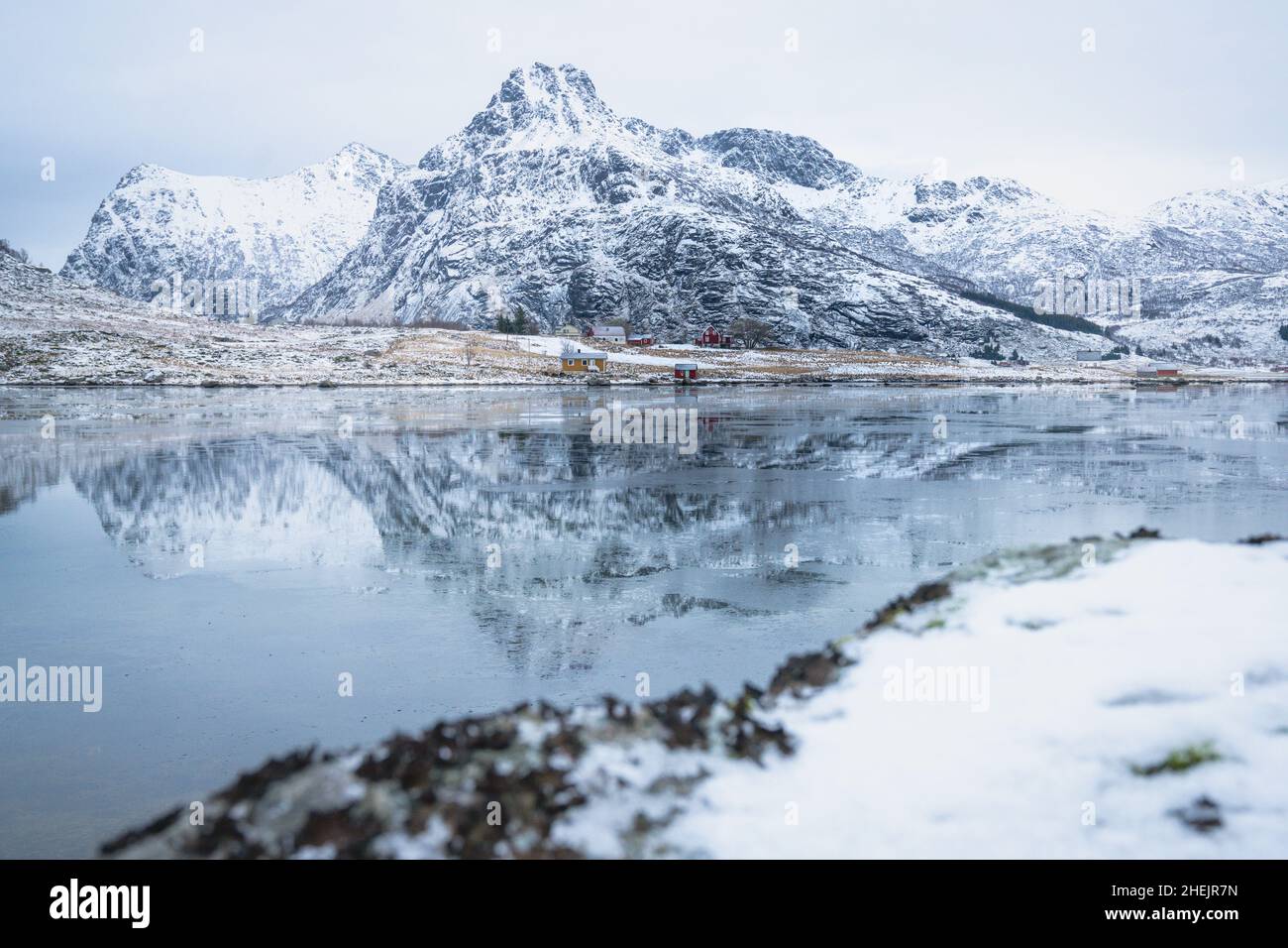 Gefrorener Fjord mit schneebedeckten Bergen, die sich im Wasser spiegeln, Flakstadpollen, Flakstadoya, Nordland, Lofoten-Inseln, Norwegen Stockfoto