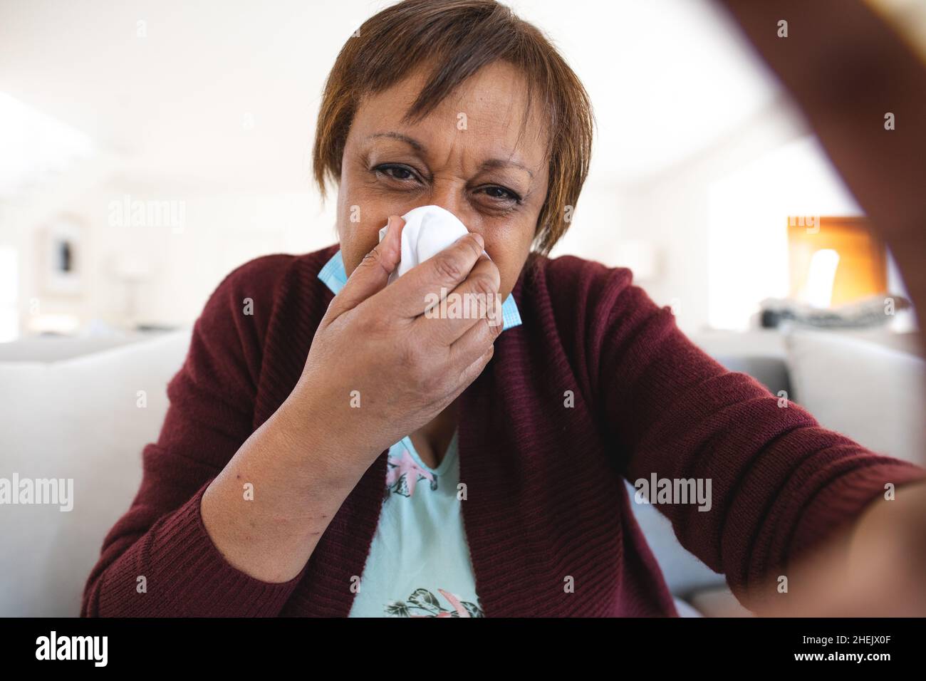 Ältere Frau, die an einer laufenden Nase leidet, nimmt zu Hause eine Online-Arztkonsultation ein Stockfoto