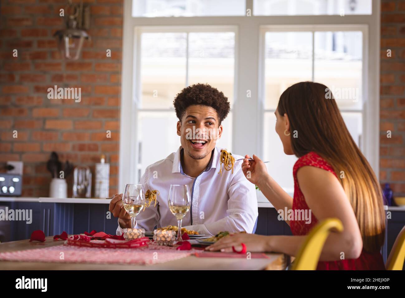 Glücklicher junger Biracial Freund und Freundin essen Spaghetti Pasta am Esstisch in der Küche Stockfoto