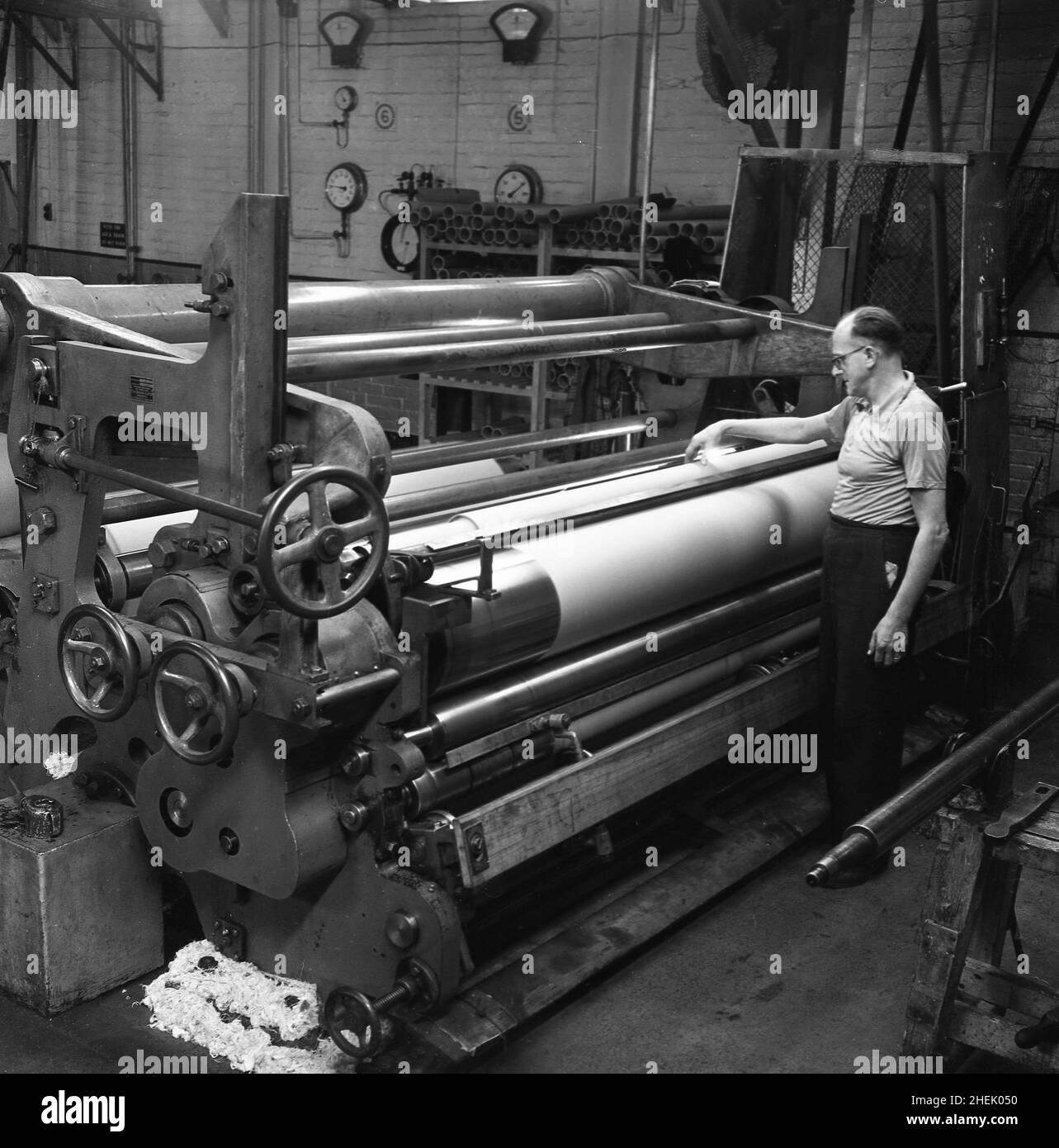 1950s, historisch, ein männlicher Arbeiter der großen Papiermaschine in der Fabrik in Brittains, Cheddleton, England, Großbritannien. In dieser Zeit war Brittains ein führender britischer Papierhersteller, dessen Geschichte bis ins Jahr 1854 zurückreicht, als sie die Nachfolge der Brüder Fourdrinier antrat, der Erfinder der ersten Papiermaschine, die ein durchgehendes Blatt Papier produzieren konnte. Thomas Brittain übernahm 1854 die Mühle der Fourdrinier Bros, der das ursprüngliche französische Design entwickelt hatte, und der Fourdrinier-Papiermaschinenbullt revolutionierte 1804 die Papierherstellung. Stockfoto
