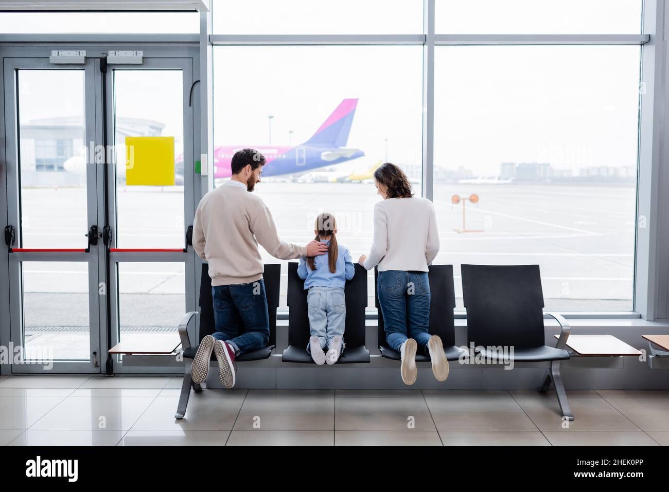 Eltern schauten ihre Tochter in der Nähe des Fensters am Flughafen an Stockfoto