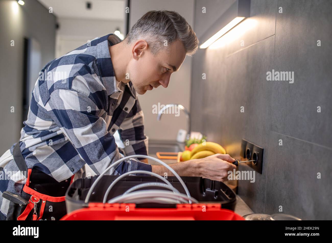 Mann seitlich zur Kamera berühren Sockel mit Schraubendreher Stockfoto