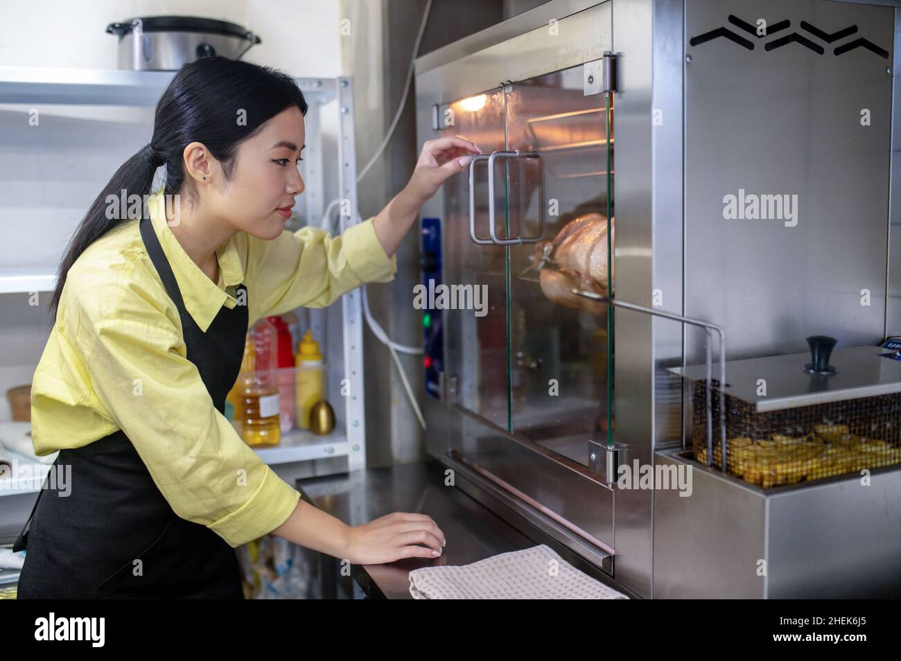 Junge asiatische Frau, die in der Küche arbeitet und die Temperatur des Backofens reguliert Stockfoto