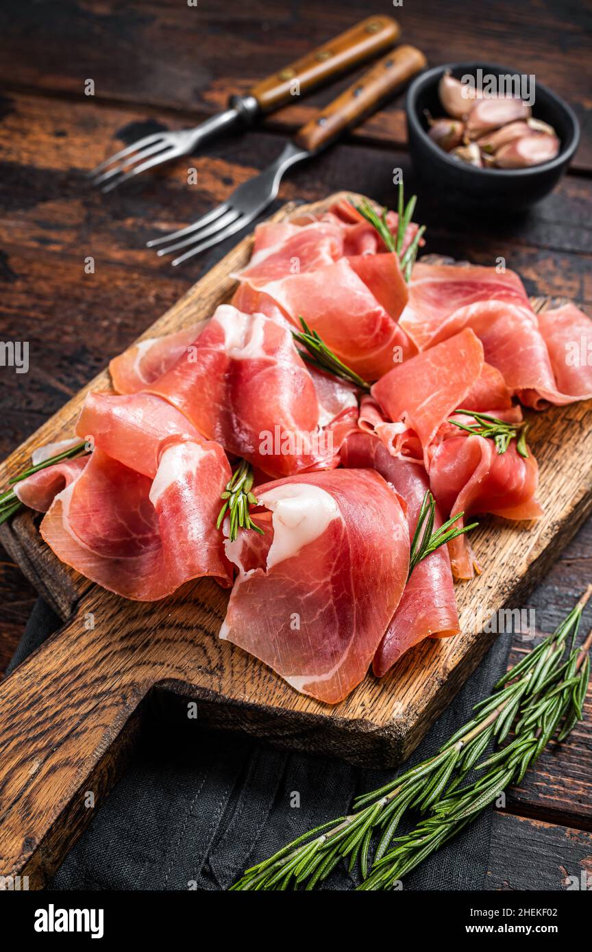 Scheiben Schinken aus Jamon serrano oder Prosciutto crudo parma auf Holzbrett mit Rosmarin. Holzhintergrund. Draufsicht Stockfoto