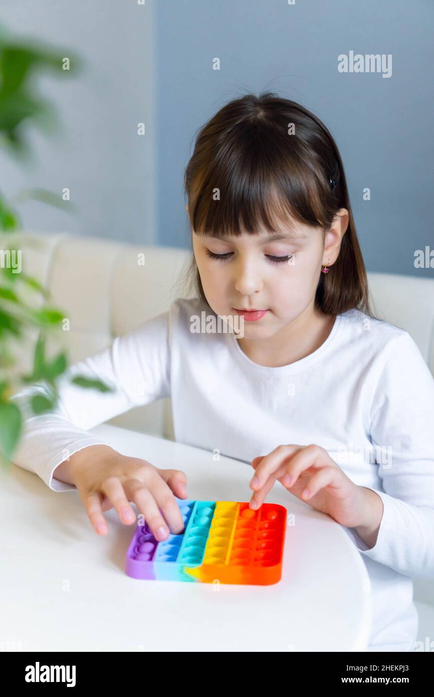 Baby Mädchen spielen mit Regenbogen Pop es fidget. Das Konzept der psychischen Gesundheit popit Spielzeug Stockfoto