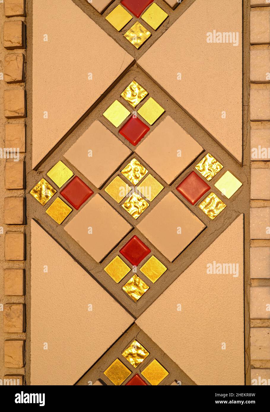 Fragment eines geometrischen, sich wiederholenden Musters aus einem Keramikmosaik an der Wand einer katholischen Kirche. Mosaikfliesen in Gold, Rot und Beige. Stockfoto